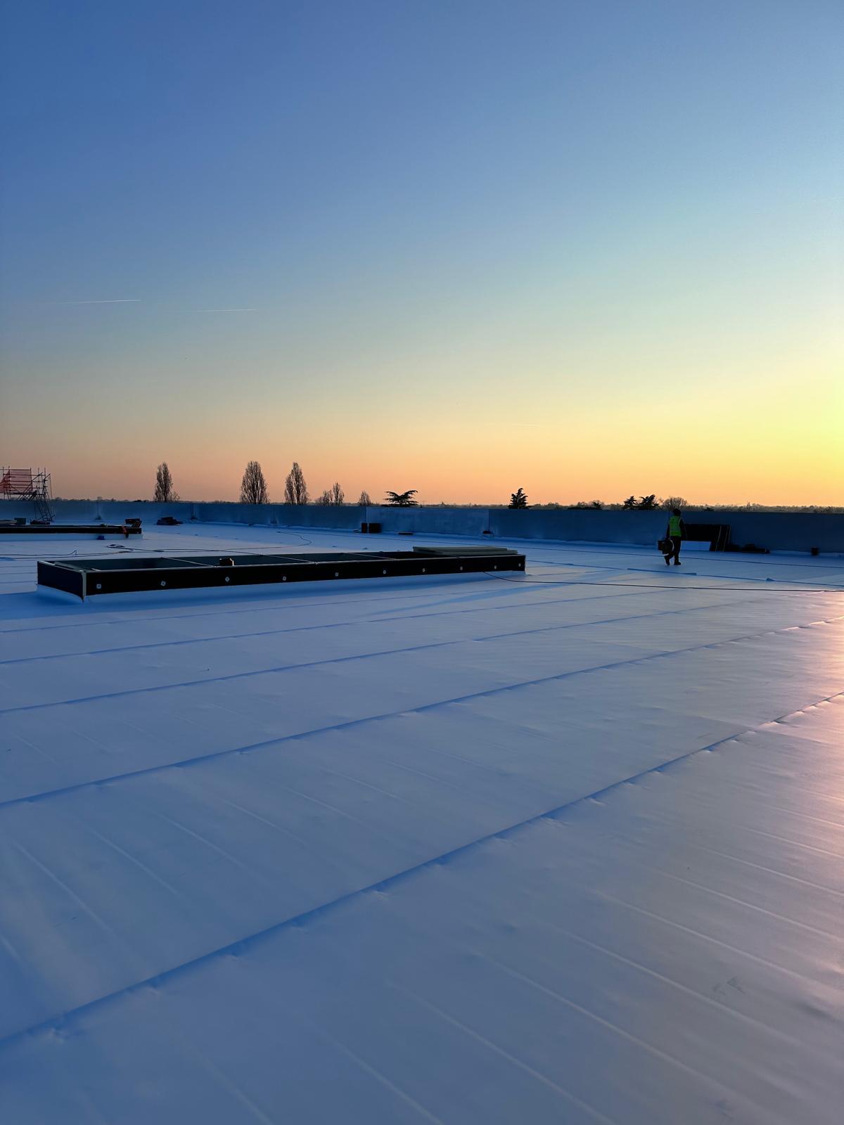 Posa di manto sintetico TPO su copertura industriale al tramonto — cantiere Industrial Services